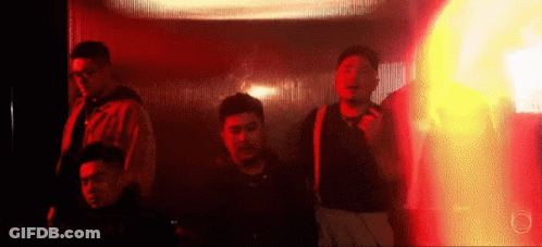 A Group Of Men Are Standing In A Dark Room With A Red Light Behind Them . GIF