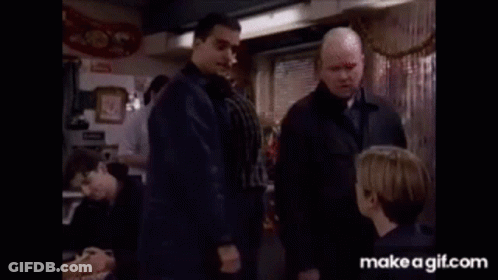 A Group Of Men Are Standing In A Restaurant Talking To Each Other And A Boy Is Sitting At A Table . GIF