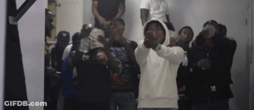 A Group Of Men Are Standing In A Room And One Of Them Is Wearing A Hoodie With The Number 18 On It . GIF