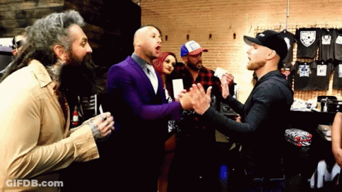 A Group Of Men Are Standing In A Room Talking To Each Other . One Of The Men Is Wearing A Purple Suit . GIF