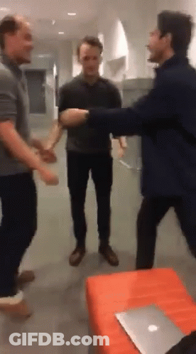 A Group Of Men Are Standing In A Room With A Laptop On The Table GIF