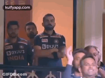 A Group Of Men Are Standing In A Room With Their Arms Crossed And Watching A Cricket Match . GIF