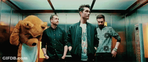 A Group Of Men Are Standing In An Elevator With A Teddy Bear In The Background . GIF