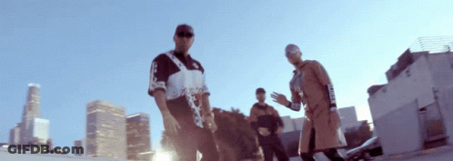A Group Of Men Are Standing In Front Of A City Skyline And One Of Them Is Wearing A Shirt That Says Supreme On It GIF