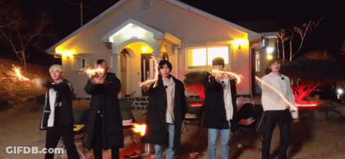A Group Of Men Are Standing In Front Of A House Holding Sparklers . GIF