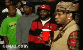 A Group Of Men Are Standing Next To Each Other In A Room . One Man Is Holding A Red Cup . GIF