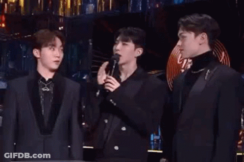 A Group Of Men Are Standing Next To Each Other On A Stage Singing Into Microphones . GIF