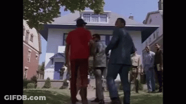 A Group Of Men Are Standing Outside Of A House Talking To Each Other . GIF
