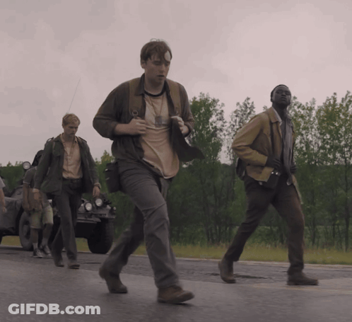 A Group Of Men Are Walking Down A Road And One Of Them Has A Badge On His Chest GIF