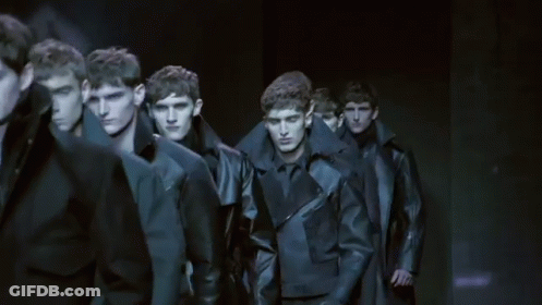 A Group Of Men Are Walking Down A Runway In A Line . GIF