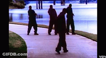 A Group Of Men Are Walking Down A Sidewalk Near A River GIF