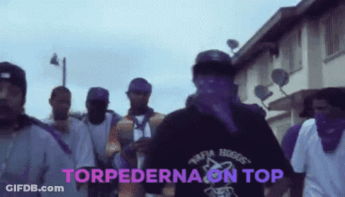 A Group Of Men Are Walking Down A Street And The Words Torpedona On Top Are On The Screen GIF