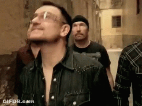 A Group Of Men Are Walking Down A Street . One Of The Men Is Wearing Glasses . GIF