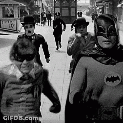 A Group Of Men Dressed As Batman And Robin Are Walking Down The Street GIF