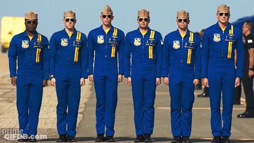 A Group Of Men In Blue Jumpsuits Are Standing In A Line With The Word Prime On The Bottom Right GIF