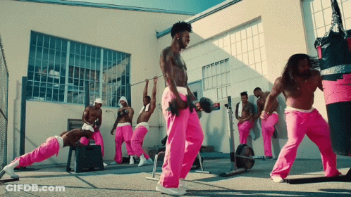 A Group Of Men In Pink Sweatpants Are Doing Exercises In Front Of A Building GIF