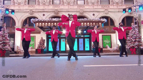 A Group Of Men In Red Jackets Are Dancing In Front Of A Building With Christmas Trees GIF