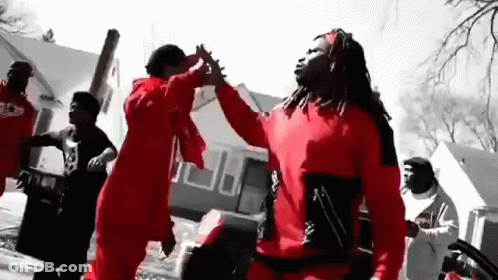 A Group Of Men In Red Shirts Are Dancing In Front Of A Building . GIF