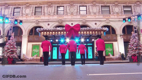 A Group Of Men In Red Uniforms Are Dancing In Front Of A Building That Says Nbc On The Front GIF
