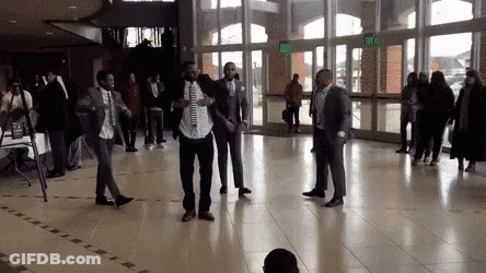 A Group Of Men In Suits And Ties Are Dancing In A Large Hallway . GIF