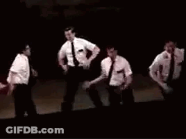 A Group Of Men In Suits And Ties Are Dancing On A Stage In A Dark Room . GIF