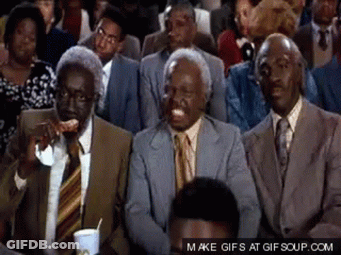 A Group Of Men In Suits And Ties Are Sitting In A Crowd And One Of Them Is Eating A Slice Of Pizza GIF