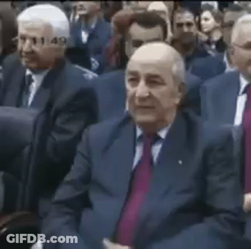 A Group Of Men In Suits And Ties Are Sitting In A Row In A Room . GIF