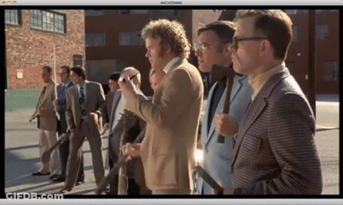 A Group Of Men In Suits And Ties Are Standing In A Row And The Screen Says Machoman GIF