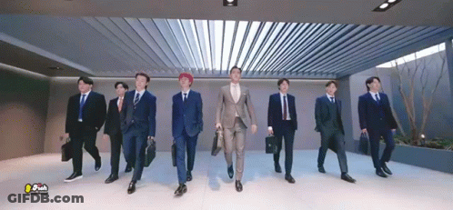 A Group Of Men In Suits And Ties Are Walking In A Hallway . GIF