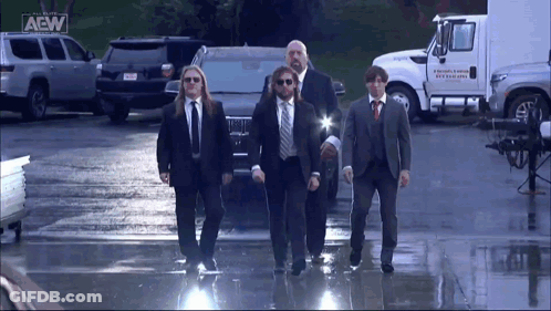 A Group Of Men In Suits And Ties Are Walking In Front Of A Truck That Says Aew On It GIF