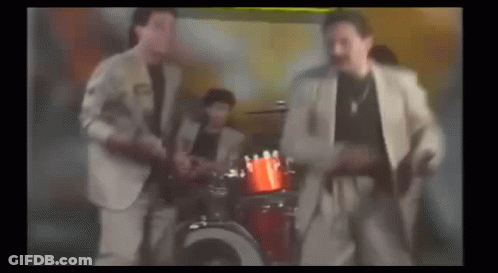 A Group Of Men In Suits Are Dancing In Front Of A Drum Set In A Room . GIF