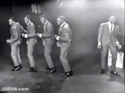 A Group Of Men In Suits Are Dancing Together On A Stage . GIF