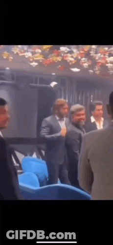 A Group Of Men In Suits Are Standing In A Dark Room . GIF