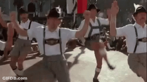 A Group Of Men In Traditional German Clothing Are Dancing Together . GIF