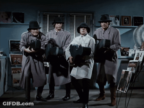 A Group Of Men In Trench Coats And Hats Are Standing In A Room Holding Cameras GIF