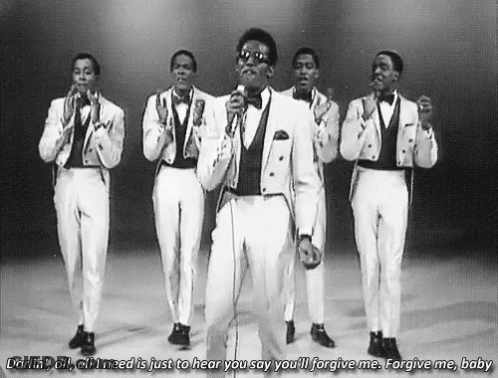 A Group Of Men In Tuxedos Are Singing Into Microphones . GIF