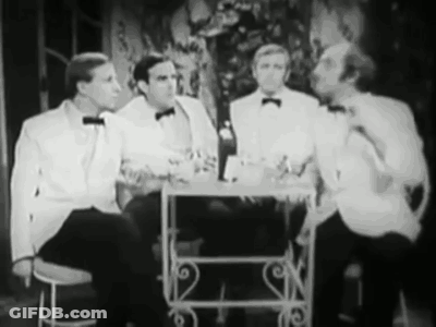 A Group Of Men In Tuxedos Are Sitting At A Table Talking To Each Other . GIF