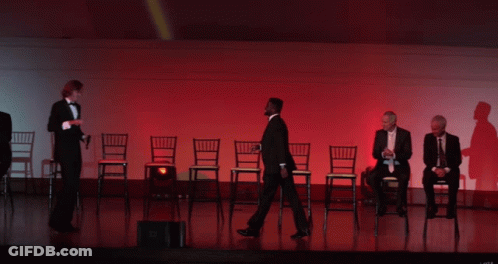 A Group Of Men In Tuxedos Are Sitting In Chairs On Stage GIF