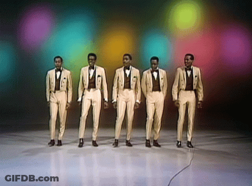 A Group Of Men In Tuxedos Are Standing In A Line GIF
