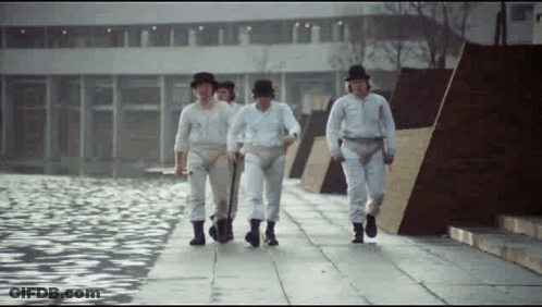 A Group Of Men In White Pants And Hats Are Walking Down A Sidewalk Near A Body Of Water . GIF