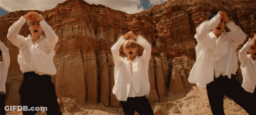 A Group Of Men In White Shirts Are Dancing In Front Of A Rocky Mountain GIF