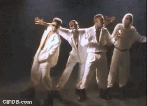 A Group Of Men In White Suits Are Dancing Together On A Stage In A Dark Room . GIF