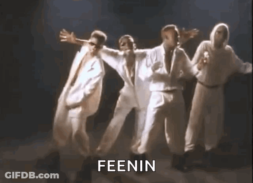 A Group Of Men In White Suits Are Dancing Together On A Stage In A Dark Room . GIF