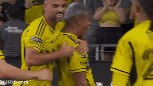 A Group Of Men In Yellow Jerseys Are Hugging Each Other . GIF