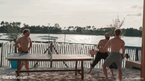 A Group Of Men Playing Ping Pong On A Beach With A Sign In The Background That Says " Attention Vehicule " GIF