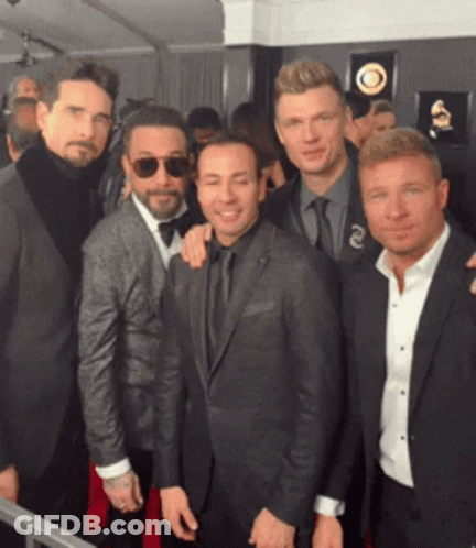 A Group Of Men Posing For A Picture With One Wearing Sunglasses And A Grammy Plaque Behind Them GIF