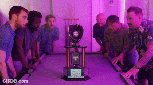 A Group Of Men Stand Around A Pool Table With A Trophy That Says Champions GIF