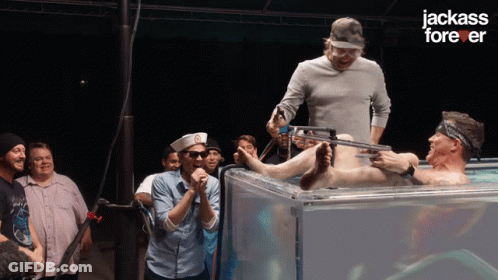 A Group Of Men Standing Around A Man In A Tank With The Words Jackass Forever On The Bottom GIF