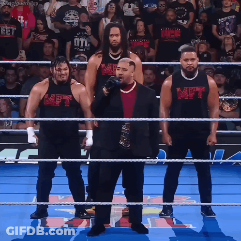 A Group Of Men Standing In A Wrestling Ring With One Wearing A Shirt That Says Met On It GIF