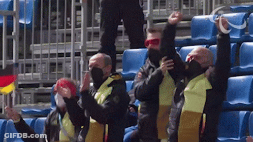 A Group Of Men Wearing Masks And Scarves Are Sitting In A Stadium With Their Arms In The Air GIF